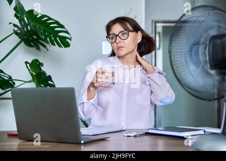 Frau mittleren Alters, die an Hitze leidet, überhitzt, durch Ventilator und Ventilator gekühlt Stockfoto