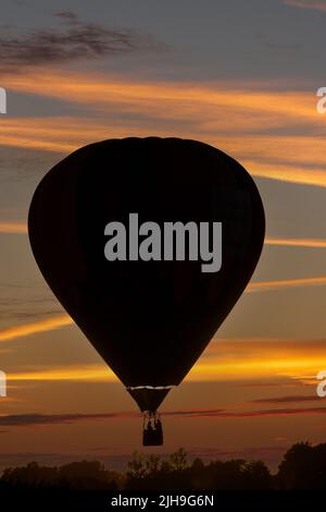 Der Heißluftballon wurde bei Sonnenuntergang in einem zusammengesetzten Bild gegen den Himmel geschildet. Stockfoto