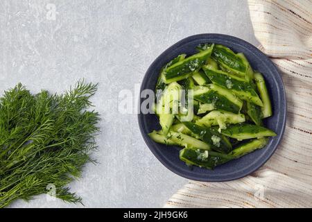 Zertrümmerte leicht gesalzene, gebrochene Gurken in einer Keramikschale, umgeben von Dill und Küchenhandtuch-Serviette. Draufsicht mit Kopierbereich Stockfoto