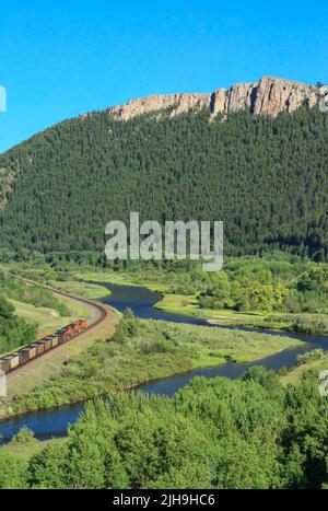 Trainieren Sie auf Eisenbahnschienen unter hohen Klippen entlang des clark Fork River Valley in der Nähe von drummond, montana Stockfoto