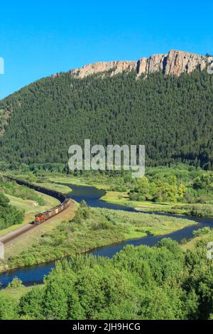 Trainieren Sie auf Eisenbahnschienen unter hohen Klippen entlang des clark Fork River Valley in der Nähe von drummond, montana Stockfoto