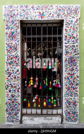 Chambranle mit traditionellen mexikanischen Gemälden mit bunten, handgemalten Figuren und Souvenirs, die an einem Metallgitter hängen und für Touristen zum Verkauf angeboten werden Stockfoto