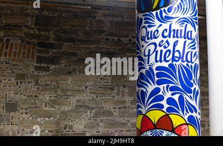 Großer Pfosten-Pilaster mit traditionellen mexikanischen talavera-Töpferwaren-Verzierungen mit der Aufschrift „qué chula es Puebla“ und einem Steinwandhintergrund Stockfoto