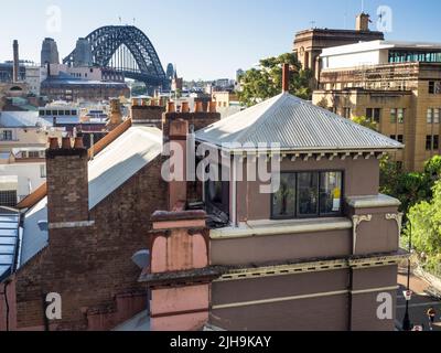 Die Sydney Harbour Bridge ragt über den Schornsteinpfannen von The Rocks, Sydneys ältestem Vorort. Das MCA ist das Art déco-Gebäude auf der rechten Seite. Stockfoto