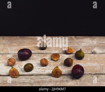 Komposition im Vintage-Stil aus Feigen, Pflaumen und Nüssen auf altem Holztisch. Dunkler Hintergrund. Retro-Food-Konzept. Stockfoto