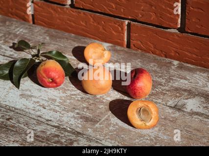 Sommerszene mit frischen Aprikosen auf Holztisch und Backstein-Hintergrund. Minimale Ästhetik. Nahaufnahme. Stockfoto