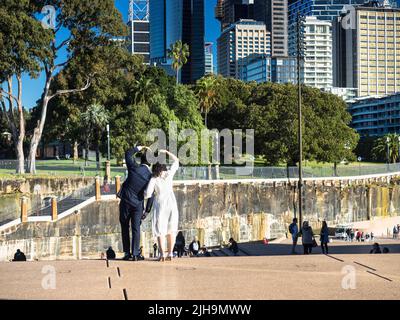 Touristen, die auf den Stufen des Sydney Opera House posieren und auf den Bennelong Lawn der Royal Botanic Gardens blicken. Stockfoto