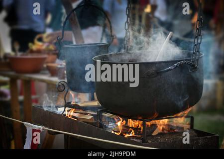 Großer Eisenkessel oder Kessel mit dampfendem Eintopf über dem Feuer, Essen für alle auf einem makellosen Fest im Freien, ausgewählter Fokus, enge Schärfentiefe Stockfoto