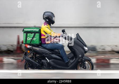 SAMUT PRAKAN, THAILAND, MAI 08 2022, Ein Motorradkurier fährt im Regen auf einer nassen Straße Stockfoto