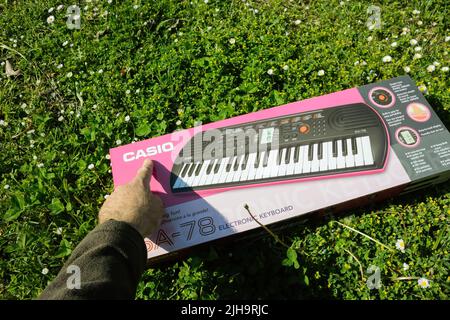 Dortmund, Deutschland - Mai 8 2022: POV männliche Hand hält neues Casio SA-78 Mini Keyboard Piano in grünem Gartengras - verweist auf den Markennamen des japanischen Unternehmens Stockfoto