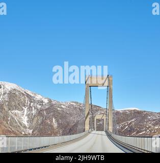 Leere Straße in den Bergen vor einem blauen Himmel mit Kopierraum. Verlassene Autobahnkreuzung in den kalten verschneiten und grauen Hügeln rund um Bodo in Norwegen Stockfoto