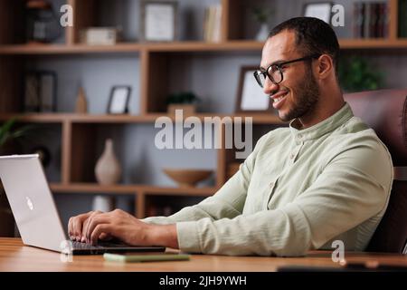 Porträt eines jungen afrikanisch-amerikanischen Geschäftsmannes, der im Büro mit einem Laptop arbeitet. Lächelnder selbstbewusster Unternehmer, der Brillen mit Computer trägt Stockfoto