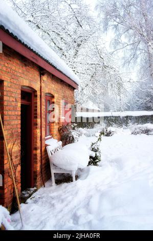 Ruhiges altes Haus in Schneelandschaft und gefrorenem Garten. Ein rotes Ziegelhaus in Europa mit einem dicken weißen, frostbedeckten Hof im Winter mit Kopierfläche Stockfoto