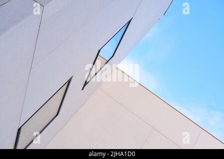 Abgewinkelte Sicht auf das Äußere eines hohen Gebäudes an einem sonnigen Tag. Konzept eines modernen weißen Gehäuses mit reflektierenden Fenstern vor einem blauen Himmel. Abstrakter Hintergrund Stockfoto