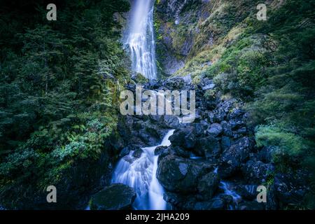 Wasserfall in den südlichen Alpen, der über die Felswand fällt und über eine felsige Basis zwischen grünem Busch und niedriger alpiner Vegetation in Arthur's Pass stürzt. Stockfoto