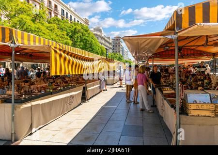 Touristen und Einheimische an Freiluftständen, die Souvenirs und Sammlerstücke auf dem Freiluftmarkt am Cathedral Place im Gotischen Viertel von Barcelona, Spanien, verkaufen. Stockfoto