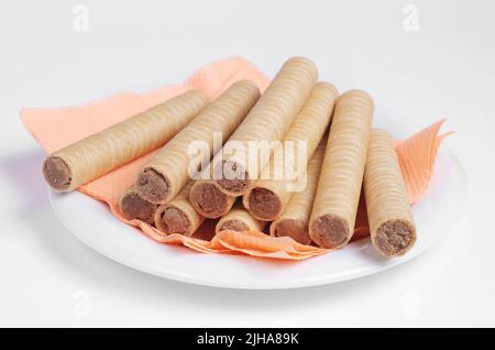 Waffelrollen mit Schokolade auf einem Teller mit einer rosa Serviette auf weißem Hintergrund. Selektiver Fokus Stockfoto