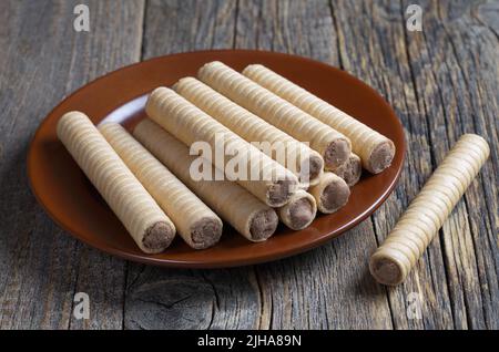 Waffelrollen mit Schokolade auf einem braunen Teller auf einem alten Holztisch Stockfoto