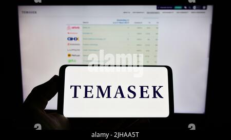 Person, die das Smartphone mit dem Logo der Firma Temasek Holdings Private Limited auf dem Bildschirm vor der Website hält. Konzentrieren Sie sich auf die Telefonanzeige. Stockfoto