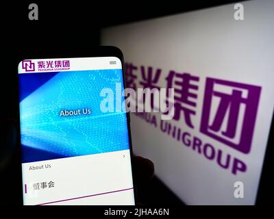 Person, die Smartphone mit der Webseite des chinesischen Konglomerats Tsinghua Unigroup vor dem Logo auf dem Bildschirm hält. Konzentrieren Sie sich auf die Mitte des Telefondisplays. Stockfoto