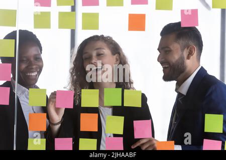 Fröhliche, multiethnische Geschäftsgruppe, die Teamarbeit genießt und Notizen ausfüllt Stockfoto