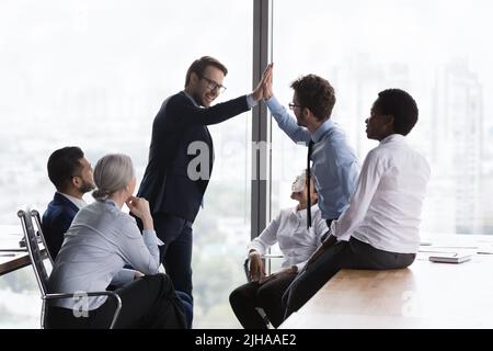 Glückliche Mitarbeiter klatschen beim Teamtreffen in die Hände und feiern den Erfolg der Gruppe Stockfoto