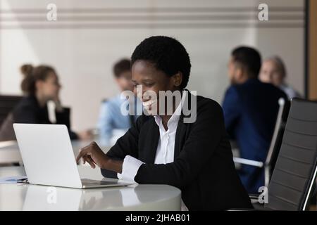 Fröhliche, glückliche, tausendjährige afrikanische Geschäftsfrau, die am Laptop arbeitet Stockfoto