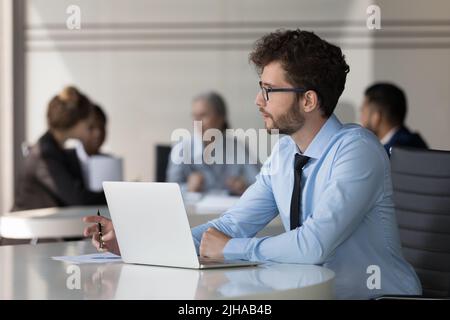Seriöse junge Geschäftsmann, der am Laptop-Computer im offenen Büro arbeitet Stockfoto