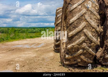 Schmutzige Doppelräder der Landwirtschaft Traktor auf unbefestigte Straße an sonnigen Sommertag mit grünen Feld im Hintergrund Stockfoto