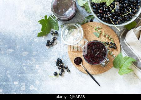 Sommerfrische-Beerenkonfitüre, hausgemachtes Konservierungskonzept. Schwarze Johannisbeerkonfitüre, Marmeladen oder Confitures mit frischen Beeren auf einer Steinplatte. Blick von Stockfoto