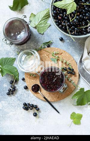 Sommerfrische-Beerenkonfitüre, hausgemachtes Konservierungskonzept. Schwarze Johannisbeerkonfitüre, Marmeladen oder Confitures mit frischen Beeren auf einer Steinplatte. Blick von Stockfoto