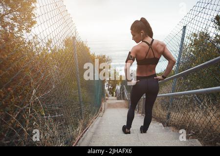Rückansicht einer muskulösen jungen Frau, die auf einer Treppe im Freien steht. Fit junge Frau, die ein körperliches Training am Morgen. Stockfoto
