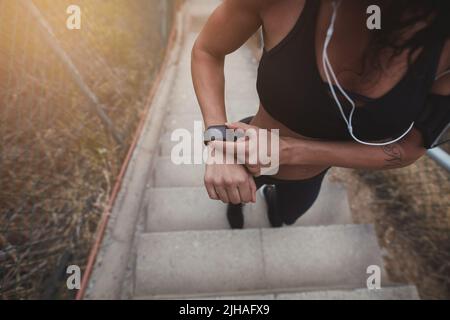 Eine sportliche Frau, die auf einer Smartwatch auf einer Treppe steht und die Zeit überprüft. Athletische junge Frau, die sich für einen morgendlichen Lauf im Freien vorbereitet. Stockfoto
