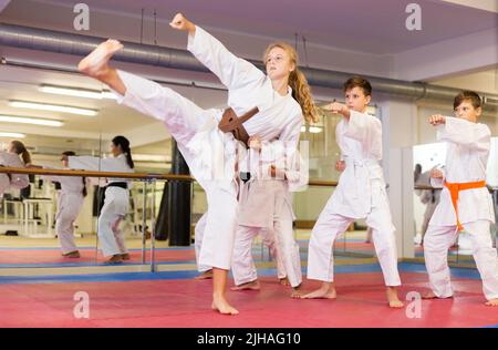 Kinder im Kimono führen Kampfbewegungen im Fitnessstudio durch Stockfoto