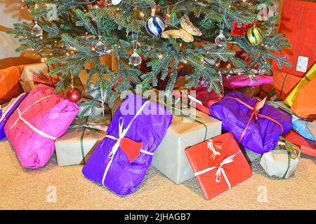 Umweltfreundliche bunte recyclebare Geschenkpapier für Weihnachtsgeschenk & Geschenkverpackung an der Basis von dekorierten künstlichen Weihnachtsbaum mit LED-Leuchten UK platziert Stockfoto