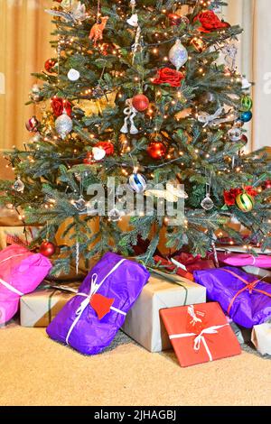 Umweltfreundliche bunte recyclebare Geschenkpapier für Weihnachtsgeschenk & Geschenkverpackung an der Basis von dekorierten künstlichen Weihnachtsbaum mit LED-Leuchten UK platziert Stockfoto