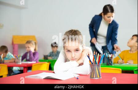 Verärgert Schulmädchen sitzt an einem Schreibtisch in Klassenzimmer Grundschule Stockfoto