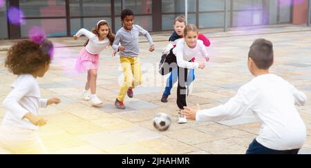 Eine Gruppe von Tweenagern, die nach dem Unterricht im Schulhof Fußball spielen Stockfoto