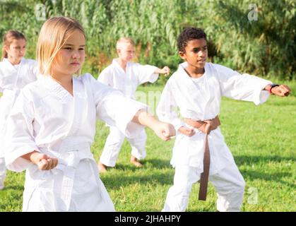 Präteen Mädchen üben Karate mit Gruppe im Sommer Park Stockfoto