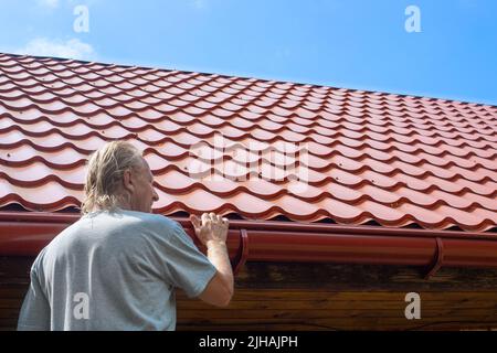 Ein Mann inspiziert eine Rinne an einem Dachabflussrohr. Ableitung von Regenwasser vom Dach. Stockfoto