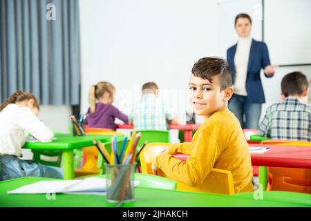 Preteen Junge Lernen im Klassenzimmer auf Hintergrund mit Klassenkameraden und Lehrer Stockfoto