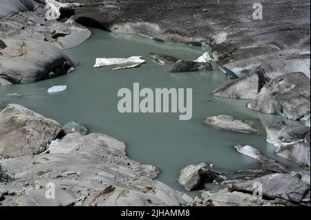 Schmelzwasserpunkt des Rhone-Gletschers, Kanton Wallis, Schweiz. Auf der rechten Seite befinden sich Eisstücke, die vom Gletscher abbrechen. Wissenschaftler geben dem durch die globale Erwärmung verursachten Klimawandel die Schuld daran, dass der sich zurückziehende Gletscher, die Quelle des mächtigen Flusses Rhone, jetzt unter dem Furka-Pass in einer Höhe von etwa 2.208 m / 7.244 ft schmilzt. Im Jahr 1850 erstreckte sich eine Eiszunge weit den Berg hinunter, bevor sie schließlich im Talbecken darunter schmelzte. Stockfoto