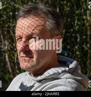Porträt eines weißen Mannes mittleren Alters mit Schatten aus den Saiten eines Tennisschlägers über seinem Gesicht Stockfoto