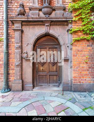 Dekorative hölzerne Bogentür, eingerahmt von gravierten Murmeln in einer roten Backsteinmauer und farbenfrohem Kopfsteinpflaster-Fliesenboden im Rathaus von Stockholm, Schweden Stockfoto