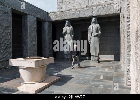 Ältere Frau, die aus dem Mausoleum von Negos herauskommt, dessen Eingang von 2 Karyatiden, modellierten weiblichen montenegrinischen Figuren, unterstützt wird.Montenegro. Stockfoto