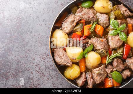 Traditioneller Fleischpeka mit Kartoffeln, Karotten, Zwiebeln, Paprika und Zucchini und Kräutern aus nächster Nähe auf dem Tisch. Horizontale Draufsicht von oben Stockfoto