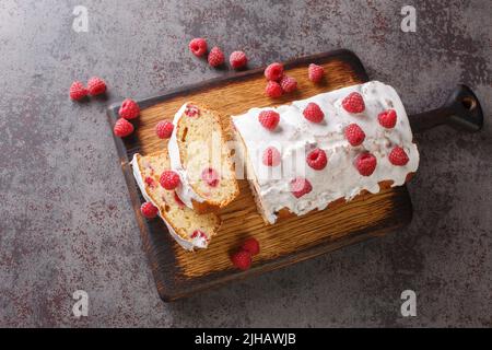 Vanillekuchen mit Himbeere und weißer Zitronenglasur aus der Nähe auf einem Holzbrett auf dem Tisch. Horizontale Ansicht von oben Stockfoto