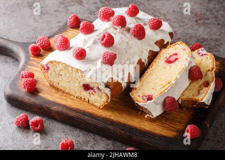 Vanillekuchen mit Himbeere und weißer Zitronenglasur in Nahaufnahme auf einem Holzbrett auf dem Tisch. Horizontal Stockfoto