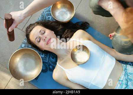 Yoga-Konzept, Meditation und Klangtherapie. Schöne junge kaukasische Frau, umgeben von tibetischen Klangschalen und Instrumenten aus Kupfer. Stockfoto