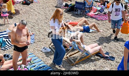 Brighton UK 17. July 2022 - Eine junge Frau trägt ihren Hund, während der Strand von Brighton voll ist, während Tausende von Besuchern die heiße Sonne genießen, da eine extreme rote Wetterwarnung für die nächsten zwei Tage im ganzen Land ausgegeben wurde : Credit Simon Dack / Alamy Live News Stockfoto